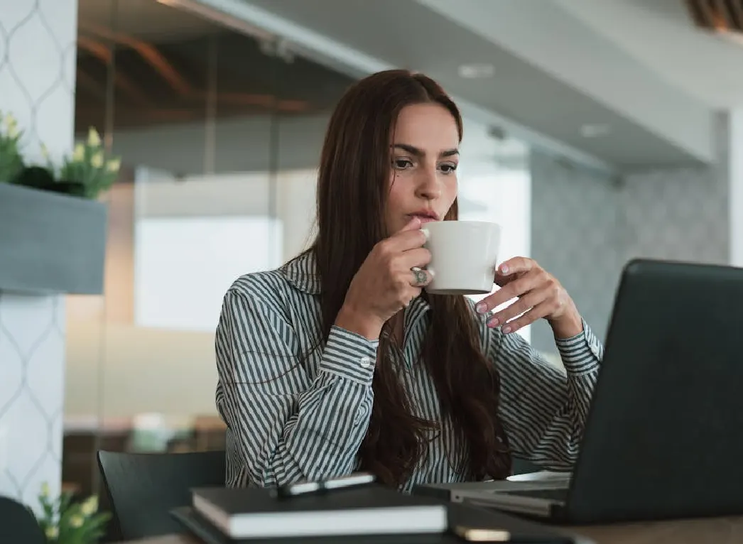 A woman sipping coffee and writing essay on her laptop